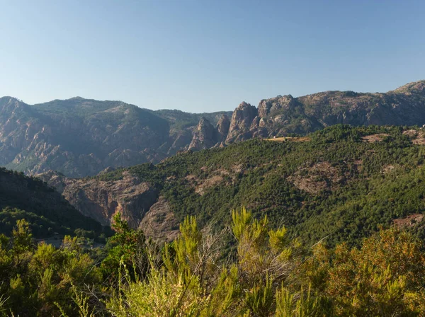 Korsika 'nın mavi gökyüzünün altındaki dağlardaki kayalar ve ormanlar üzerinde ışık etkisi