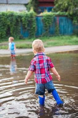 Lastik botlarla su birikintilerinde koşan mutlu çocuk. Çocuk yağmurdan sonra su sıçratır...
