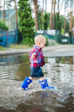 Lastik botlarla su birikintilerinde koşan mutlu çocuk. Çocuk yağmurdan sonra su sıçratır...