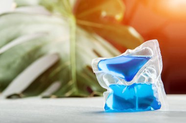 Mavi çamaşır kapsülü ve canavar yaprağı arka planında kopyalama alanı. Yoğunlaştırılmış deterjan ve temizlik...