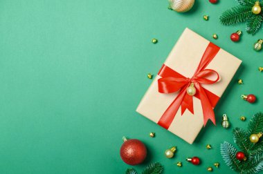 Kırmızı kurdeleli Noel hediyesi kutusu, yeşil arka planda, firavun dalları ve süslemeleri ile..