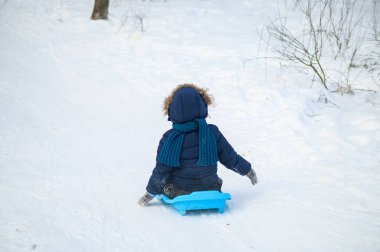 Küçük çocuk karlı ormanda kızakla kayarken dışarıda eğleniyor. Aktif çocukluk, mevsimlik açık hava eğlencesi, kış macerası, aile eğlencesi ve sağlıklı yaşam tarzı konsepti..