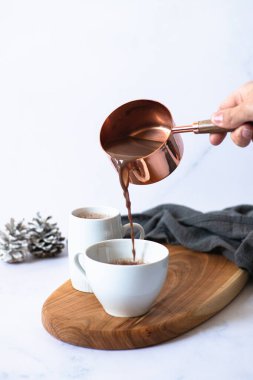 İki beyaz fincanda sıcak çikolata ya da tahta bir tahta üzerinde kakao içmek açık mermer arka planda şenlikli kış süslemeleri. Kadın eli bardağa su dolduruyor. Kış havası. Seçici odak 