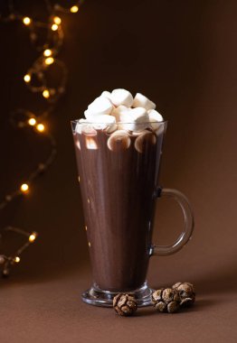 Kahverengi arka planda bir bardakta marşmelov ve şenlikli kış süslemeleri olan kakao içeceği. Kış havası. Minimalist monokrom kompozisyonu. Seçici odaklanma. Ön manzara. Dikey. Boşluğu kopyala 