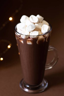 Kahverengi arka planda bir bardakta marşmelov ve şenlikli kış süslemeleri olan kakao içeceği. Kış havası. Minimalist monokrom kompozisyonu. Seçici odaklanma. Ön manzara. Dikey. Boşluğu kopyala 