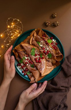 Yeşil bir tabakta servis edilen çikolatalı krep ya da kızılcık ve fındıklı krep. Kış tatili kahvaltı konsepti. Noel ve yeni yıl kahvaltısı. Tabak tutan kadın elleri
