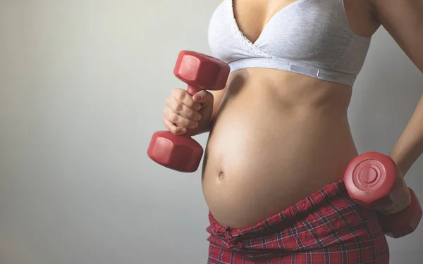 Pregnant woman holding sports dumbbells in her hands. Sports during pregnancy. Maternal prenatal care. Maternity, pregnancy, baby expectation concept. Second trimester of pregnancy. Copy space