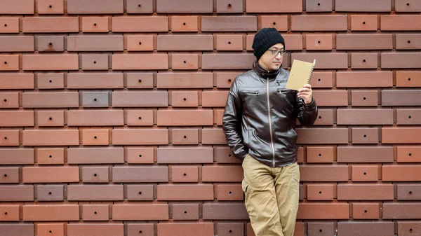 Un hombre asiático en una chaqueta marrón con un cuaderno pequeño — Foto de Stock