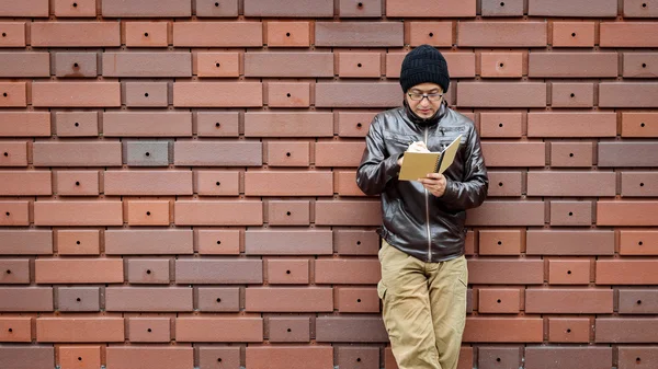 Un hombre asiático en una chaqueta marrón con un cuaderno pequeño — Foto de Stock