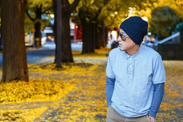 An asian man in a polo t-shirt walks in a street in autumn — Stock Photo, Image