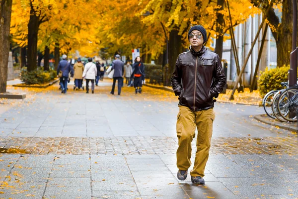 Ein asiatischer Mann in brauner Jacke spaziert im Herbst durch einen Park — Stockfoto