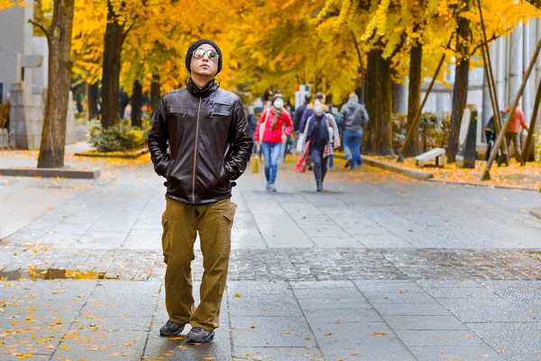 Un hombre asiático con una chaqueta marrón pasea en un parque en otoño — Foto de Stock