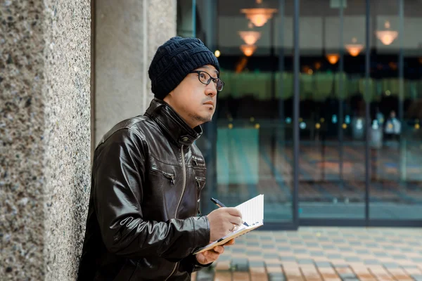 Ein asiatischer Mann in brauner Jacke mit kleinem Notizbuch — Stockfoto