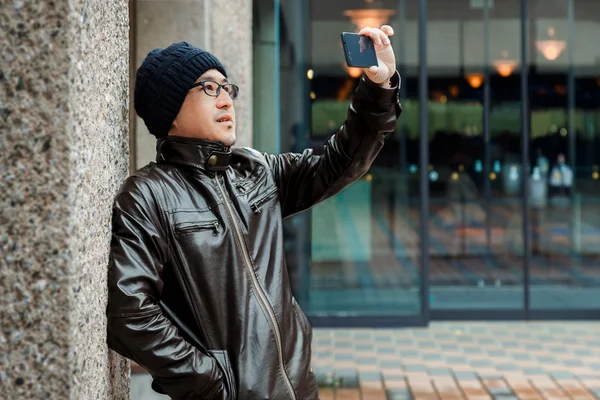 Ein asiatischer Mann in brauner Jacke mit seinem Smartphone — Stockfoto
