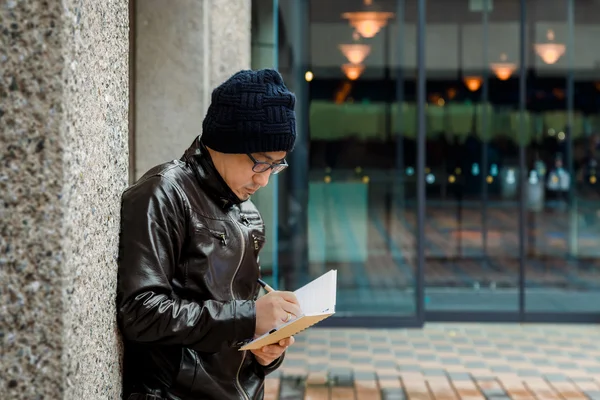 Азиатский человек в коричневой куртке с маленькой записной книжкой — стоковое фото