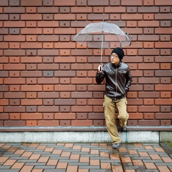 Ein asiatischer Mann in brauner Jacke mit durchsichtigem Regenschirm — Stockfoto