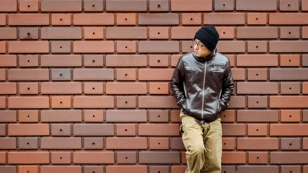 Азиат в коричневой куртке прислоняется к стене — стоковое фото