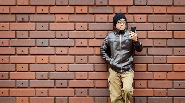 Un hombre asiático en una chaqueta marrón con su Smartphone — Foto de Stock