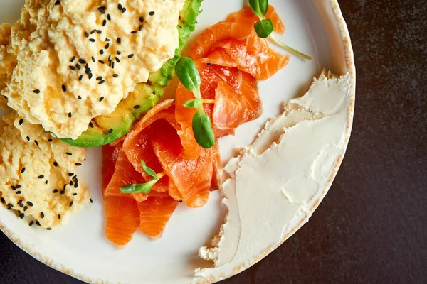 Perfect breakfast - scrambled eggs with salmon, avocado and cream cheese in a white plate. Selective focus