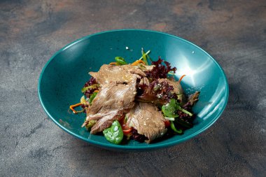 Sulu biftekli salata, siyah arka planda bir tabakta otlar ve domatesler