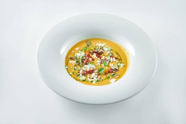 İştah açıcı balkabağı kremalı çorba, beyaz bir tabakta beyaz arkaplanda kurutulmuş domates ve mikroyeşil.
