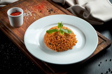 İştah açıcı ve sağlıklı bir meze. Kırmızı soslu bulgur. Arka planda beyaz bir tabakta Türk baharatı.