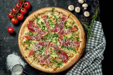 Peynirli İtalyan pizzası, prosciutto, roka ve parmesan karışımı ve siyah arka planda malzemeler.