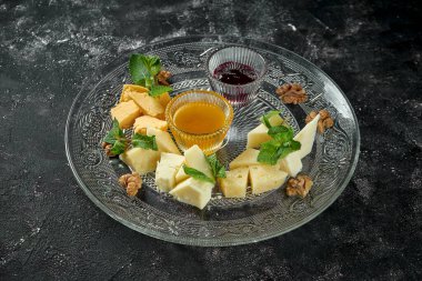 Mükemmel aperatif. Koyu arkaplanda şeffaf bir tabakta bal ve fındıklı çeşitli ev yapımı peynirler.