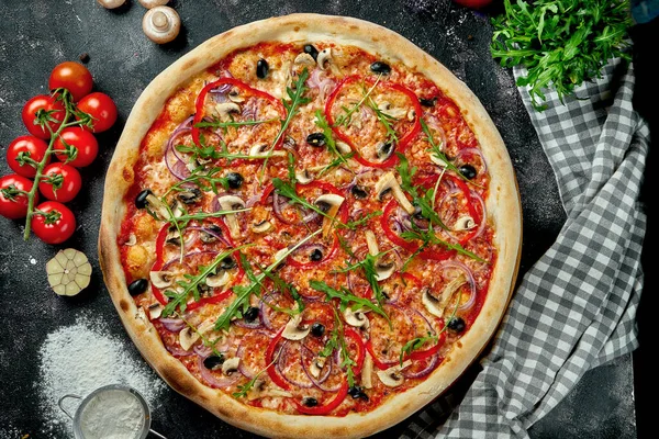 Oven-baked Italian pizza with sauce, cheese, mushrooms, bell peppers and olives in a composition with ingredients on a dark background. Top view. Vegetarian pizza