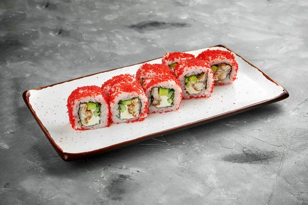 Classic sushi california roll in tobiko caviar with eel, cucumber and cream cheese on a white plate on a gray background. Close up, selective focus