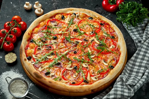 Oven-baked Italian pizza with sauce, cheese, mushrooms, bell peppers and olives in a composition with ingredients on a dark background. Top view. Vegetarian pizza