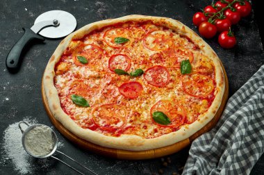 Peynirli, domatesli, fesleğenli ve kırmızı soslu İtalyan pizzası siyah arka planda malzemelerle birlikte. Pizza margarita.