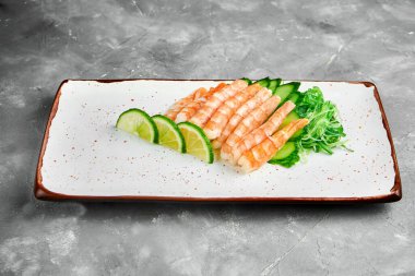 Klasik Japon saşimi seti. Limonlu çiğ karides. Beyaz bir tabakta salatalık. Yaklaş, seçici odaklanma