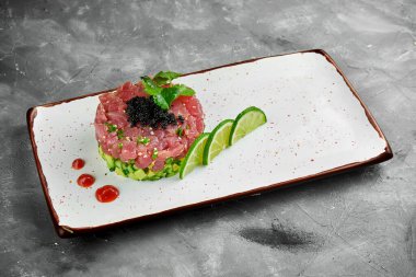 Lezzetli aperatif. Avokado ve siyah havyarlı ton balığı. Gri arka planda beyaz bir tabakta..