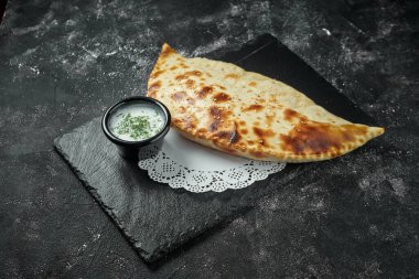 Chebureki, koyu arkaplandaki siyah tabakta öğütülmüş et ve soğan dolu, bol yağda kızartılmış bir turta. Yantyk, Kırım Tatar mutfağının yemeğidir.