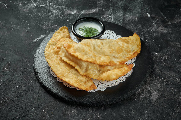 Chebureki is a deep-fried turnover with a filling of ground or minced meat and onions on black slate plate on dark background. Chebureki is dish of Crimean Tatar cuisine