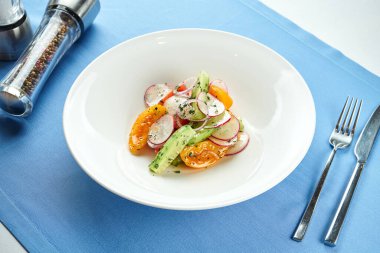 Taze ve hafif sebze salatası domatesler, salatalıklar ve turplar mavi masa örtüsü üzerinde beyaz bir tabakta..