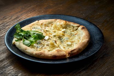 Ahşap arka planda siyah bir tabakta servis edilen 4 çeşit peynirli ve beyaz soslu ahşap pizza. Bir çeşit İtalyan pizzası.