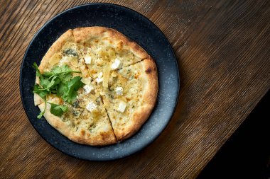 Ahşap arka planda siyah bir tabakta servis edilen 4 çeşit peynirli ve beyaz soslu ahşap pizza. Bir çeşit İtalyan pizzası.