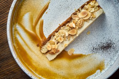 Klasik bir dilim peynirli kek, badem ve karamel soslu, beyaz bir tabakta servis ediliyor. Restoran yemeği. İştah açıcı tatlı