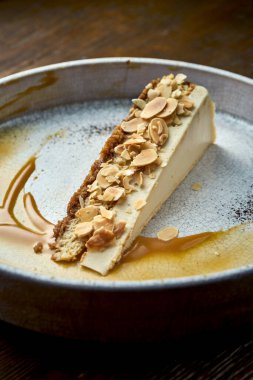 Klasik bir dilim peynirli kek, badem ve karamel soslu, beyaz bir tabakta servis ediliyor. Restoran yemeği. İştah açıcı tatlı