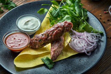 İştah açıcı bir Türk mutfağı. Pide ekmeği, kişniş, soğan ve soslu kıymalı tavuk kebabı. Ahşap bir zeminde mavi bir tabakta servis ediliyor. Restoran yemeği. Görüntüyü kapat
