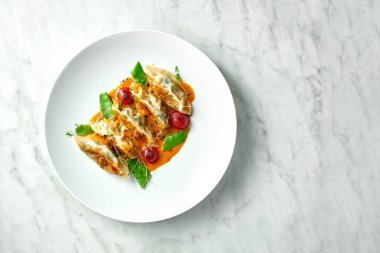 Kızarmış hamur köftesi veya sarı soslu Japon Gyoza, vişneli domates ve yeşil bezelye, mermer arka planda beyaz bir tabakta servis edilir. Pan-Asya mutfağı. Restoran yemekleri.