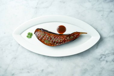 Josper 'da fırında patlıcan, miso sosu, kişniş, fındık ve susam tohumu. Miso patlıcan, beyaz bir tabakta mermer bir arka planda. Yukarıdan görüntüle