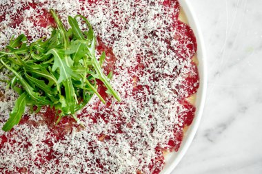 Klasik İtalyan aperatifi. Mermer bir zeminde beyaz bir tabakta servis edilen roka ve parmesanlı dana carpaccio. İnce dilimlenmiş biftek..