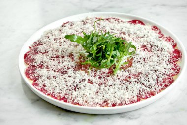 Klasik İtalyan aperatifi. Mermer bir zeminde beyaz bir tabakta servis edilen roka ve parmesanlı dana carpaccio. İnce dilimlenmiş biftek..