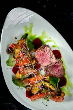 Beyaz tabakta servis edilen, sebze garnitürlü orta pişmiş sığır eti madalyonları. Koyu mermer arka plan. Barbekü et, restoran yemeği. Lezzetli biftek.