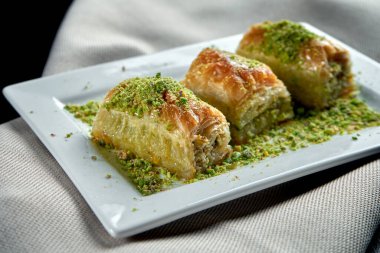 Klasik Türk tatlıları, ballı baklava ve beyaz tabakta puf böreğinden fıstık. Yaklaş, seçici odaklanma