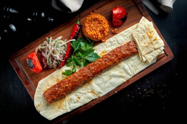 Tahta tahtada ızgara sebzeli, soğanlı ve pirinçli ızgara Türk kuzu lula kebabı. Koyu arkaplan.