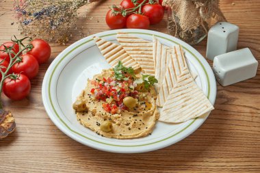 Klasik bir oryantal meze tabağı. Beyaz zeytinyağı ve sebze salsa sosuyla bezelye humusu. Ahşap bir arka planda, siyah bir tabakta servis ediliyor. Restoran yemekleri.
